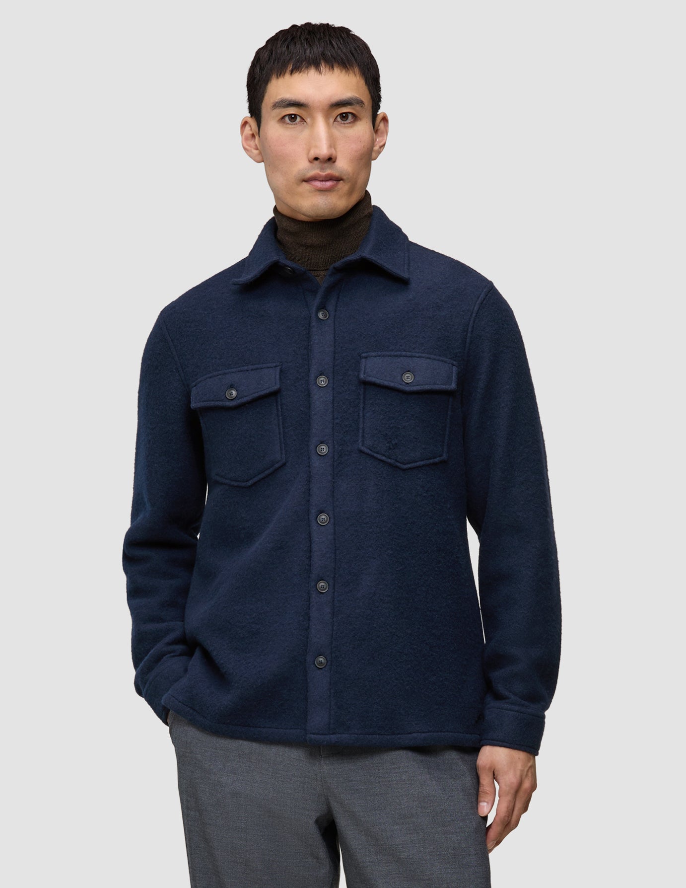 En mann har på seg en dobbeltsidig ullskjorte i mørk marineblå i standardpassform over en brun turtleneck, noe som gjenspeiler et minimalistisk design.